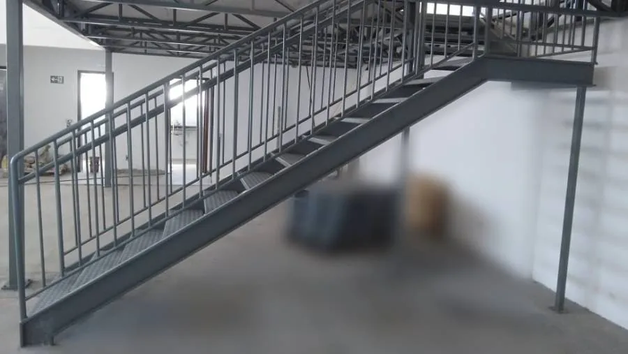 Escada metálica longa com patamar e guarda-corpo instalada sob um mezanino